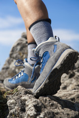 Close up of hiking boots and legs climbing up rocky trail and reaching the top of a mountain
