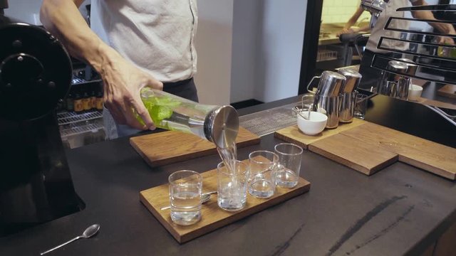 Unrecognizable barista is pouring mint water from transparent bottle to four glass on serving plate in atrisan cafe shop