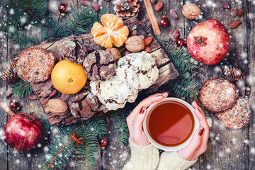 Female hand a cup of tea. Christmas Cookies Chocolate, tea, pomegranate, Tangerines, Nuts, cocoa beans on wooden snowy background. Christmas and Happy New Year card. Top view, selective focus