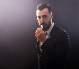 Man using an advanced personal vaporizer or e-cigarette, close up; low-key image.