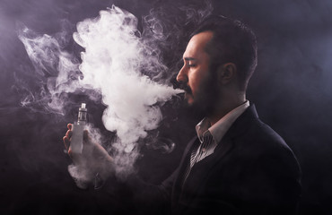 Man using an advanced personal vaporizer or e-cigarette, close up; low-key image.