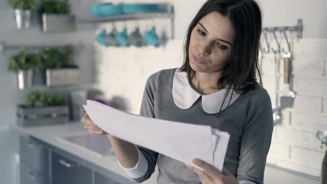 Sad, overwhelmed businesswoman working with documents standing in kitchen
