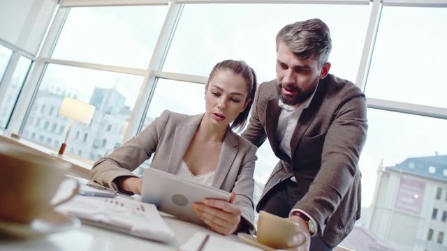 Female CEO and businessman discussing something on screen of digital tablet at office table