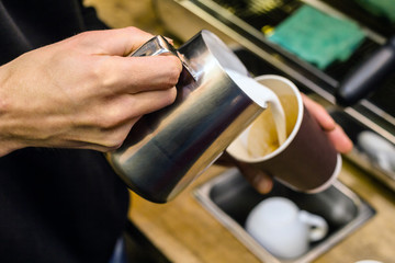 Barista pouring milk to takeaway coffee.