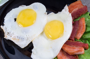 Top view on black plate with fried eggs, bacon and lettuce