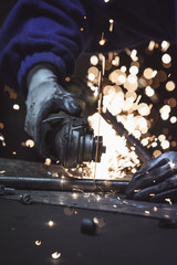 Industrial worker cutting metal pipe with many sparks baubles in the background
