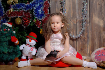 little girl in pink dress sitting by the Christmas tree decorated and waiting for when Christmas...