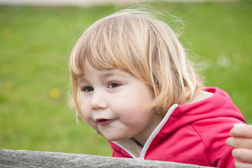little blonde cute child sitting looking at and eating bread piece with green grass background 
