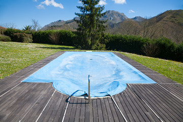 swimming pool with wooden curb closed and covered with blue tarp in Spring green meadow rounded by...