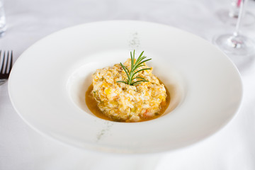 elegant white circular bowl plate with scrambled egg with cod and fish, decorated with green rosemary leave, on white tablecloth in restaurant
