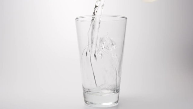 SLOW MOTION: Clear water pour into a transparent glass on a white background