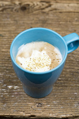 Cup of hot frothy cappuccino coffee sprinkled with sugar and spices and served in a colorful blue mug