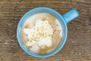 Tasty creamy cup of cappuccino coffee garnished with a sprinkling of spices viewed from above on a rustic table