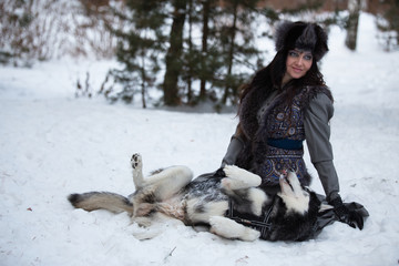 Attractive young woman playing with husky dog lying on the snow
