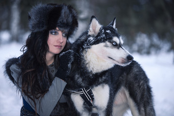 Young attractive woman with husky dog looking aside in snowing park