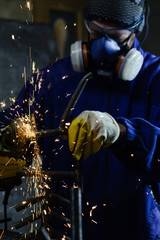 Obraz na płótnie Canvas Industrial worker producing hot sparks while grinding steel metal pipe in workshop
