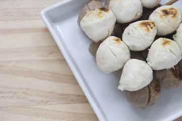 Pork meatballs on white plate placed on a wooden floor.