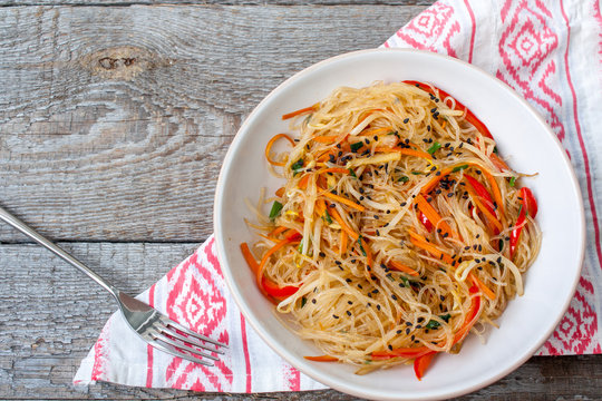 Rice noodles with vegetable stir fry on the ceramic bowl on dark wooden background