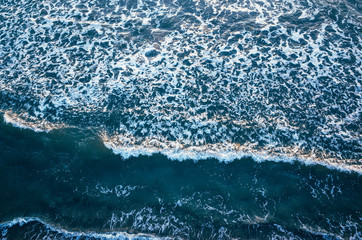 Aerial view of the tidal waves reaching the empty sandy beach  in winter