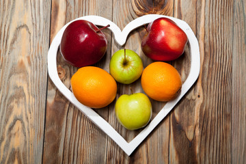 White heart, apples and oranges on the wooden background