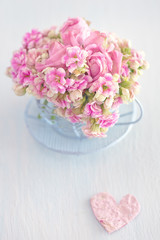 Lovely bunch of a pink flowers in a vase ,decorated with a heart on a table .