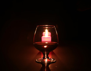 Brandy glass and candles on black background