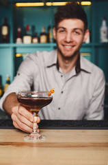 Young Barman offers alcohol cocktail in night club bar