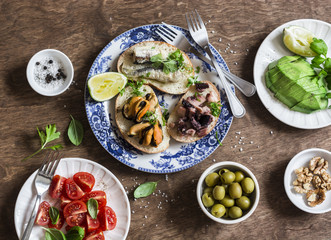 Delicious tapas - sandwiches sardines, mussels, octopus, grape, olives, tomato and avocado on wooden table, top view. Flat lay