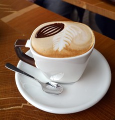 Delicious foamy cappuccino on a white cup on a plate.