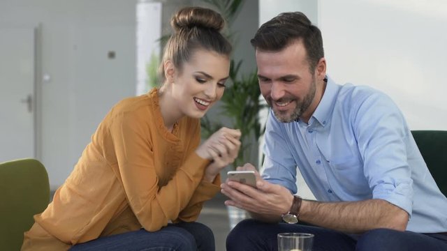 Happy couple browsing smartphone during meeting at cafe
