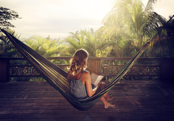 woman in a dress reading book in a hammock in the jungle at sunset