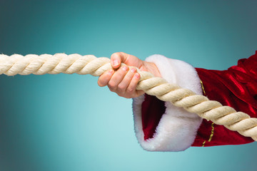 Hand of Santa Claus pulling the rope on blue background