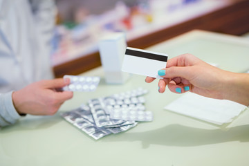 Close-up view of female hand holding credit card and pharmacist gives tablets