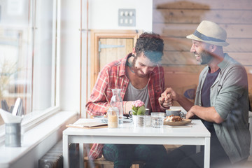 Gay couple sat holding hands in cafe