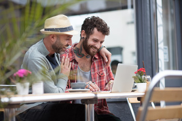 Gay couple sat sharing laptop outside cafe