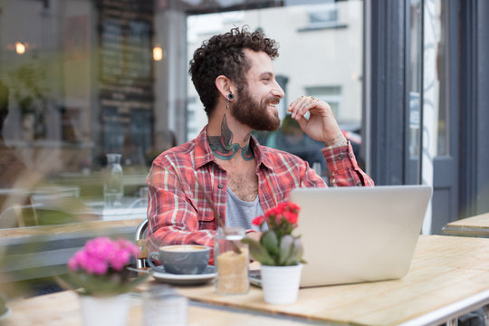 Young tattooed hipster using his laptop, sat outside a cafe
