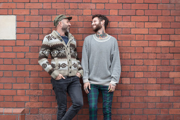 Gay couple lent against a brick wall, laughing
