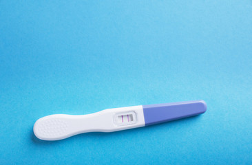 Pregnancy test positive with two stripes. Plastic cover on blue.