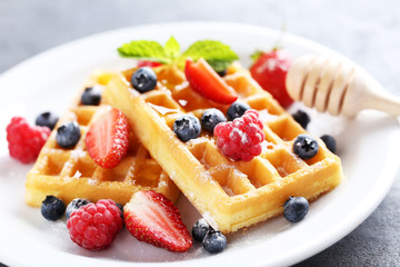 Homemade waffles with berries in plate on grey table