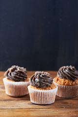 Close view at tasty chocolate cup cakes over wooden background. Vertical shot. Copy space.