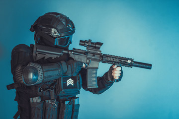 Member of the SWAT squad with an assault rifle in a black uniform on blue background. Special...