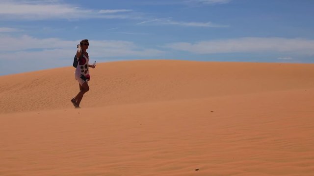 Young woman walking across the sand dunes and drinking water from bottle

