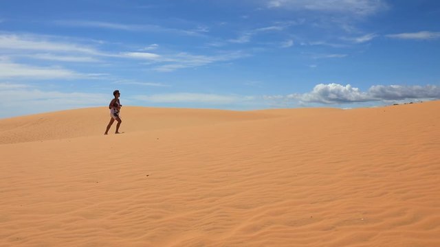 Young woman walking across the red sand dunes and drinking water from bottle
