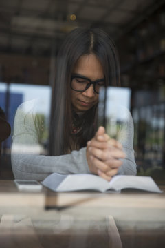 Beautiful woman wearing glasses Sitting in a coffee shop, laid hands on the book with a serious expression.