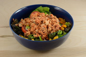 Salmon salad in blue bowl made with red leaf lettuce, bell peppers, tomatoes, onions and canned wild caught sockeye salmon