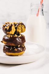 Fresh baked gluten free chocolate donuts and bottle of milk on white table