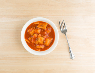 Bowl of ravioli on a wood table with fork.