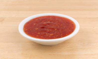 Chili chicken sauce portion in a small bowl atop a wood table.