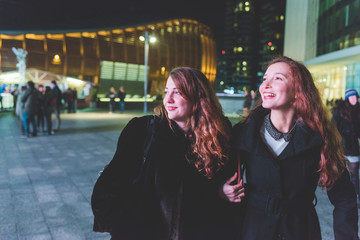 Two young beautiful caucasian women walking outdoor in the city evening, having fun interacting - friendship, interaction, having fun concept