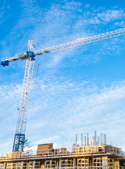 High-rise building under construction. The site with crane against blue sky with white clouds.